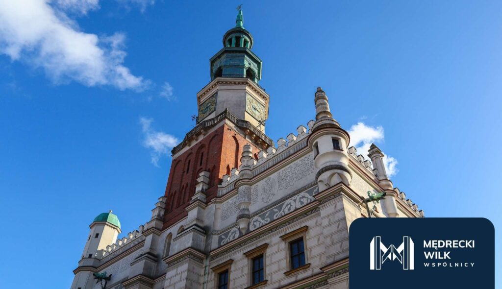 kancelaria-frankowa-poznan – Kancelaria Mędrecki Wilk i Wspólnicy  Wieża ratusza w Poznaniu sfotografowana z dołu na tle niebieskiego nieba. W prawym dolnym rogu znajduje się logo kancelarii Mędrecki Wilk i Wspólnicy.