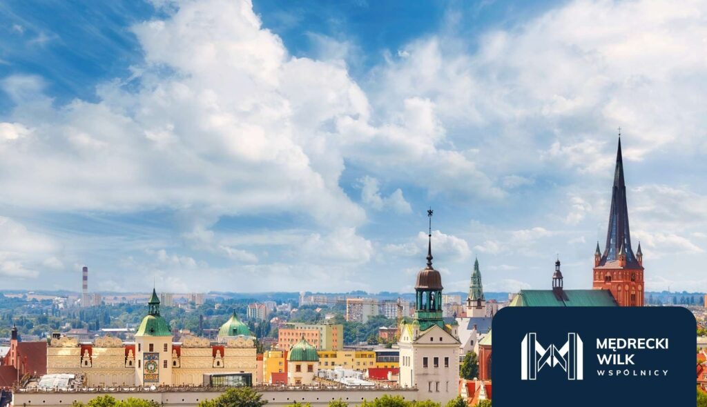 kancelaria-frankowa-szczecin – Kancelaria Mędrecki Wilk i Wspólnicy Panorama Szczecina z widokiem na czerwone i zielone dachy, wieże kościołów i budynki centrum. W prawym dolnym rogu logo kancelarii Mędrecki Wilk.