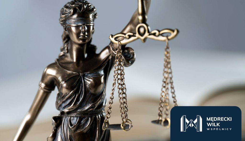 Figura Temidy z wagą sprawiedliwości w dłoni, symbol prawa i bezstronności. W prawym dolnym rogu logo kancelarii Mędrecki Wilk i Wspólnicy.