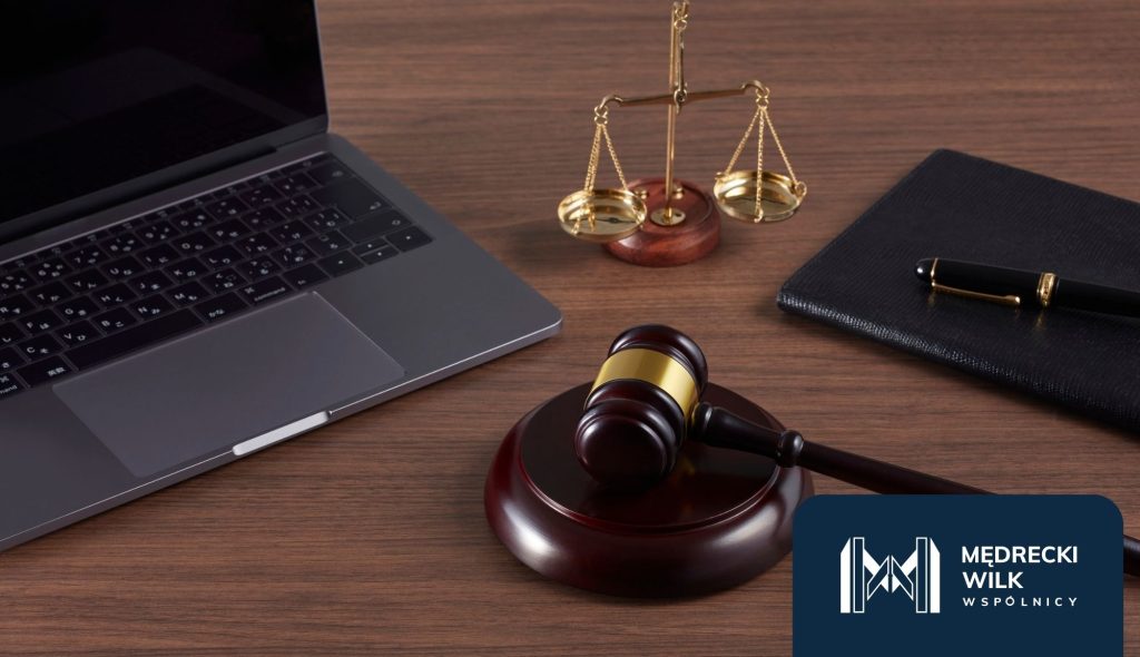 Biurko prawnika – laptop, młotek sędziowski, waga sprawiedliwości oraz notes z piórem.