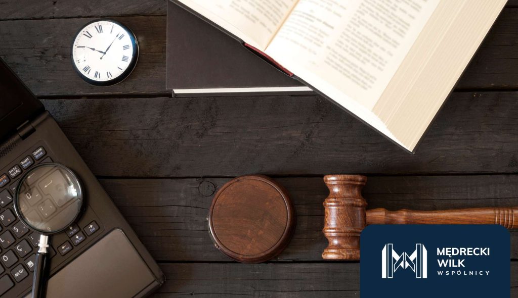 Rzut zgóry na biurko, na którym znajduje się sędziowski młotek, laptop, ksiązka, lupa