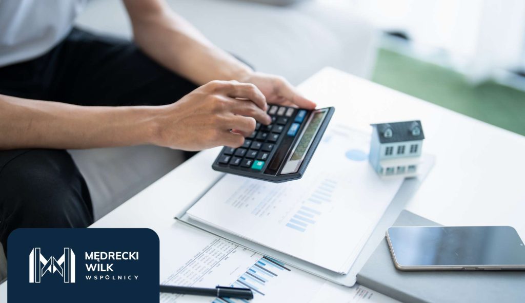 Dłonie z kalkulatorem, na stole umowa kredytowa, telefon i makieta domku