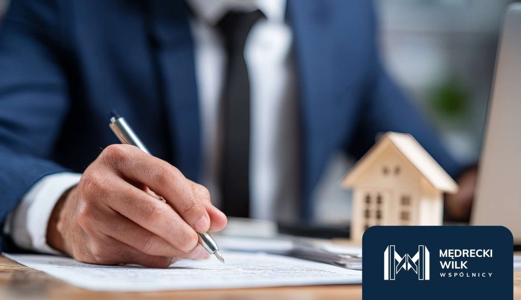 Podpisanie umowy, mężczyzna w garniturze składający podpis, obok drewniana makieta domku