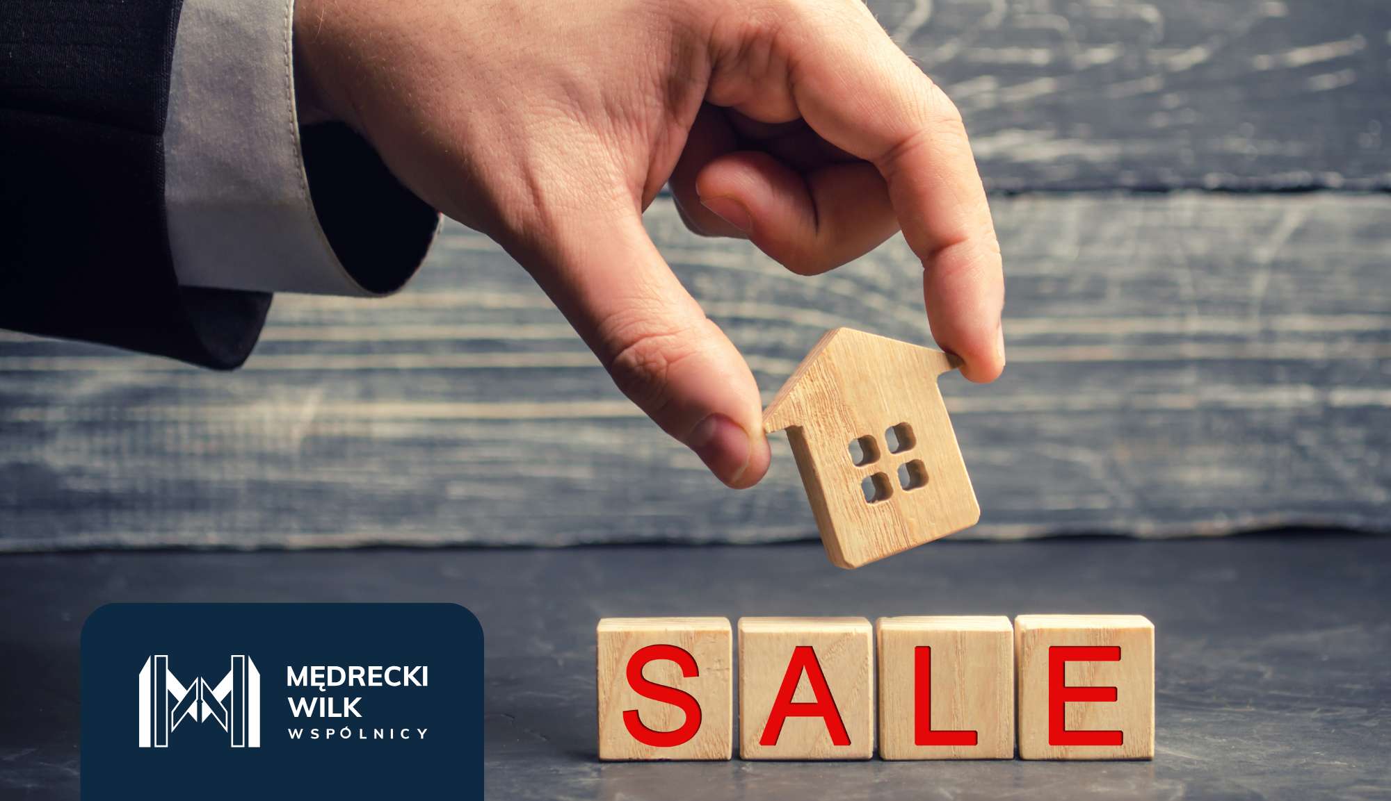 Dłoń trzymająca drewnianą figurkę domu, w tle napisz "SALE"