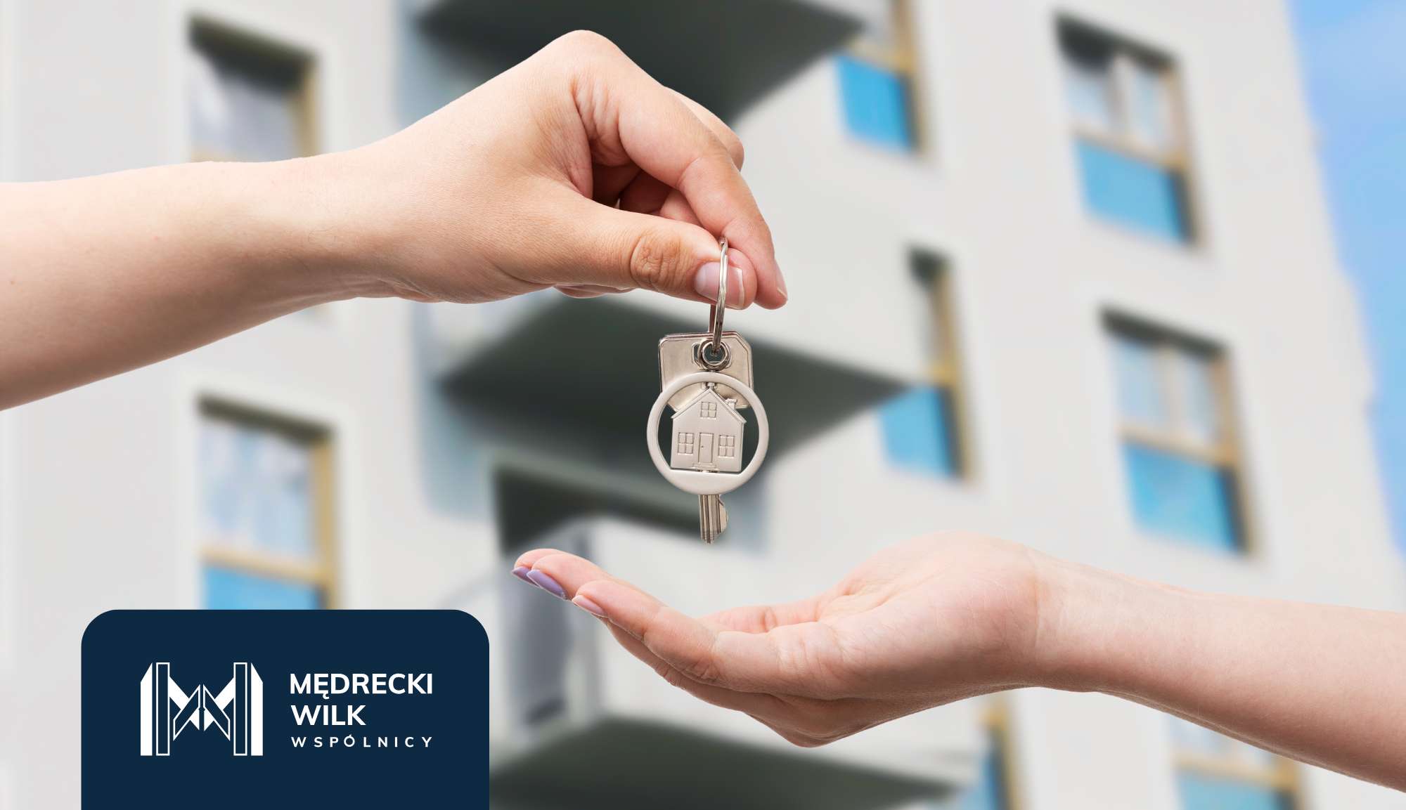 Jedna dłoń podająca drugiej klucze do mieszkania, w tle blok
