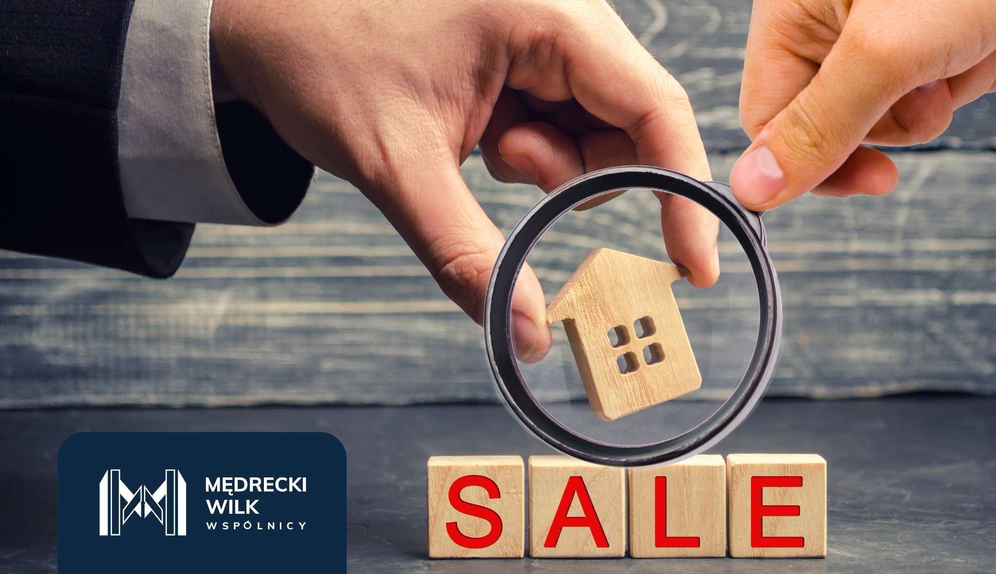 Dłoń trzymająca drewnianą figurkę domu, w tle napisz "SALE"