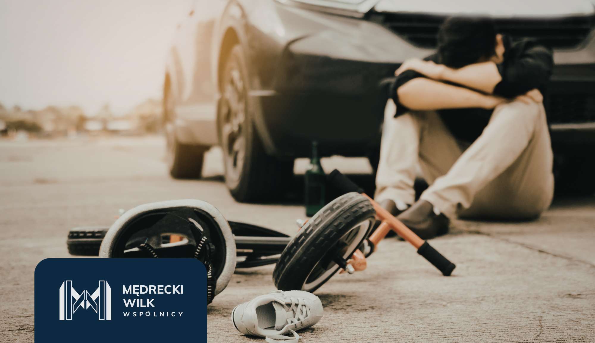 Person sits on the ground beside a car after a bicycle crash, with the bike parts scattered nearby and a bottle on the ground behind them, indicating an accident scene.