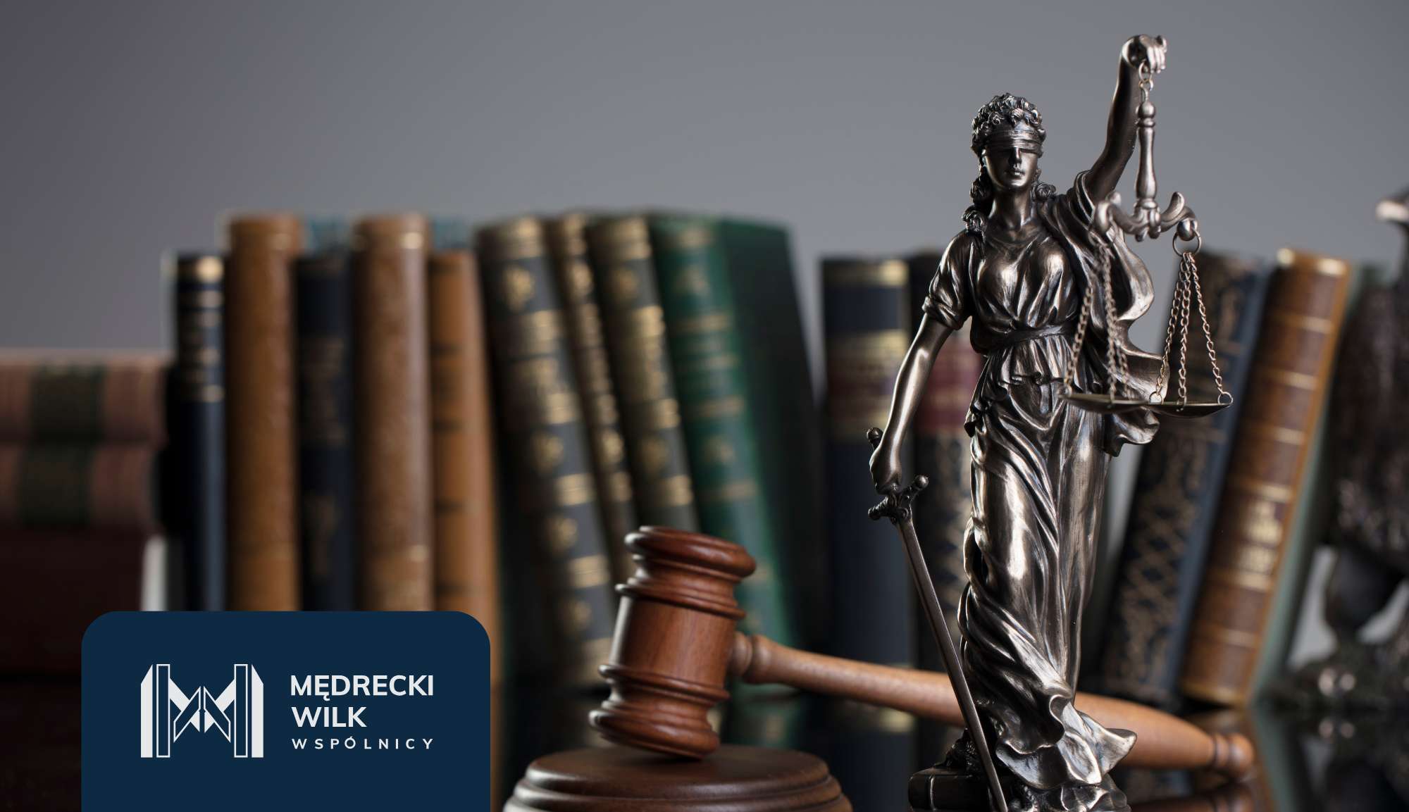 Statue of Lady Justice holding scales with a gavel nearby and law books in the background; includes a dark blue logo overlay in the corner.