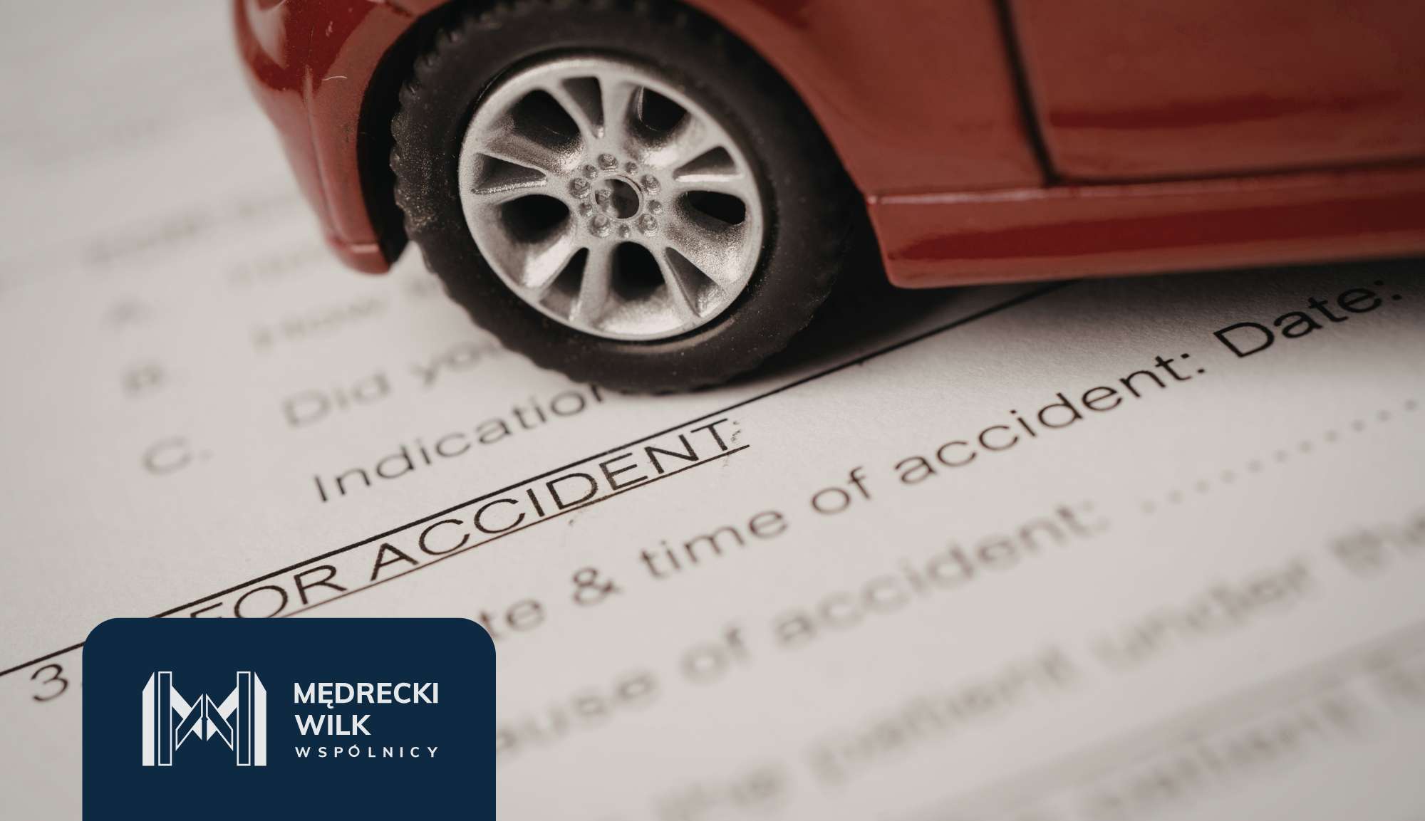 Red toy car resting on an accident claim form, with a blue Mędrecki Wilk logo in the corner, highlighting insurance documentation.