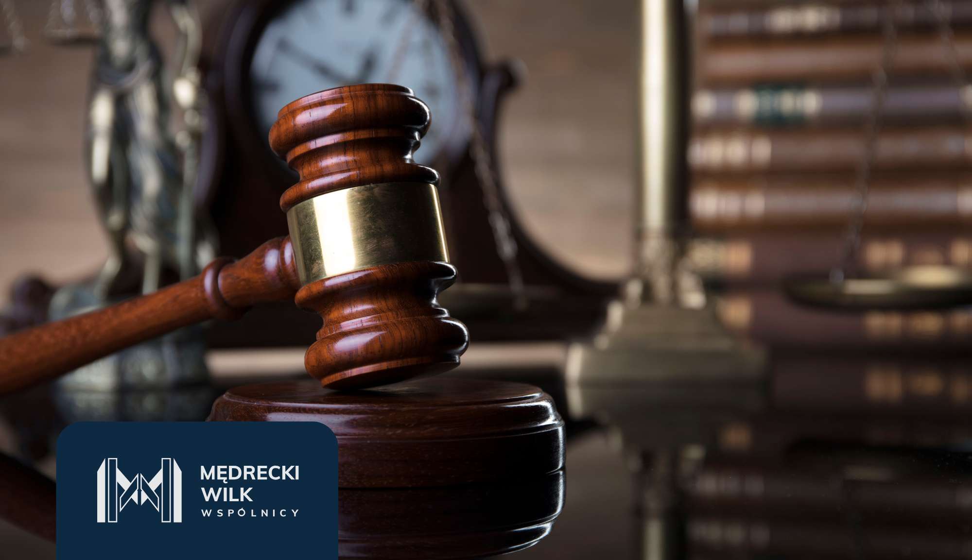 Close-up of a wooden judge's gavel resting on a desk with a blurred courtroom background and a dark blue logo in the bottom-left corner.