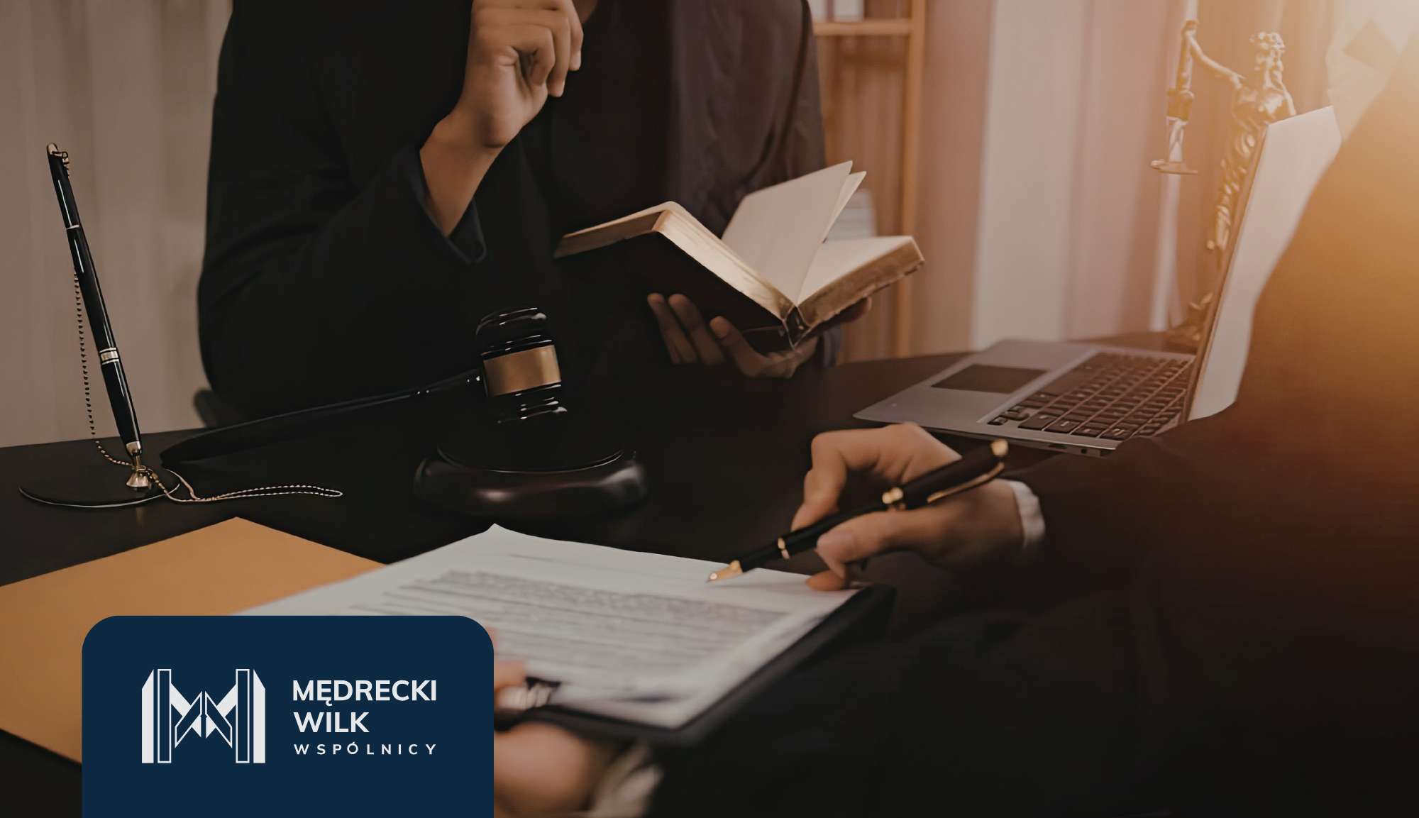 Law office scene with a person in a dark suit reading an open book at a desk next to a laptop, gavel, and documents.