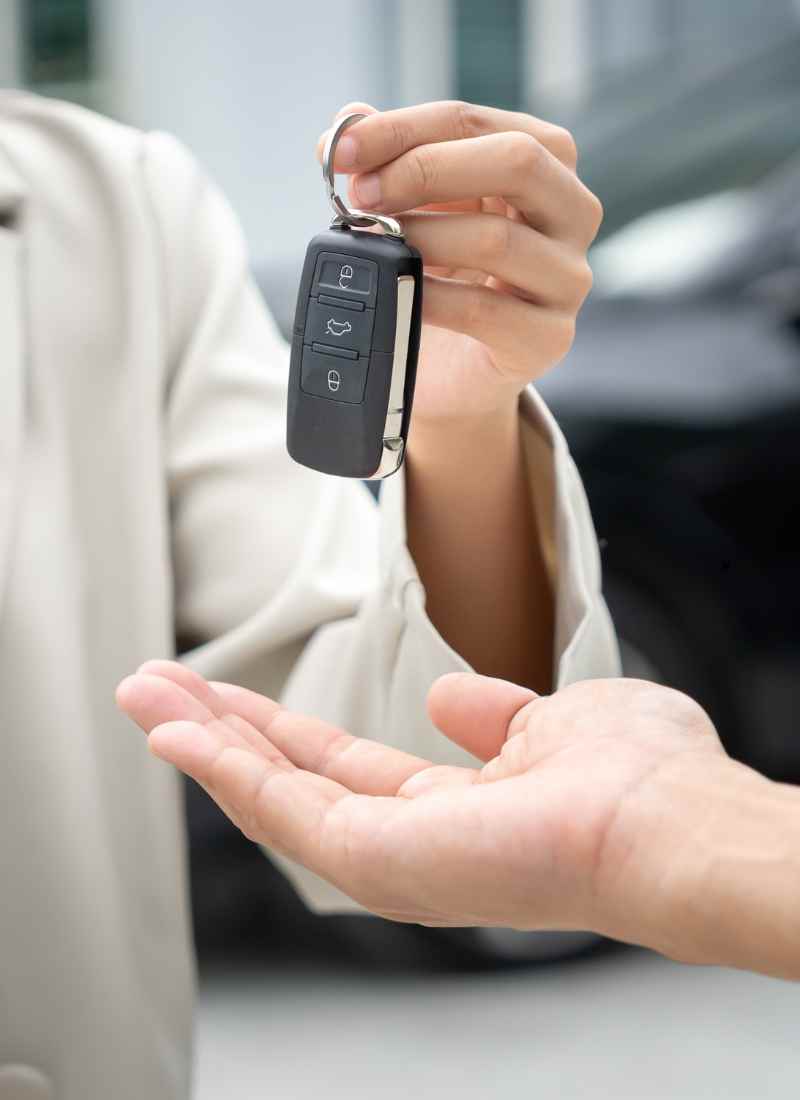 Person hands a car key fob to another person, grip visible with ring and buttons on the fob