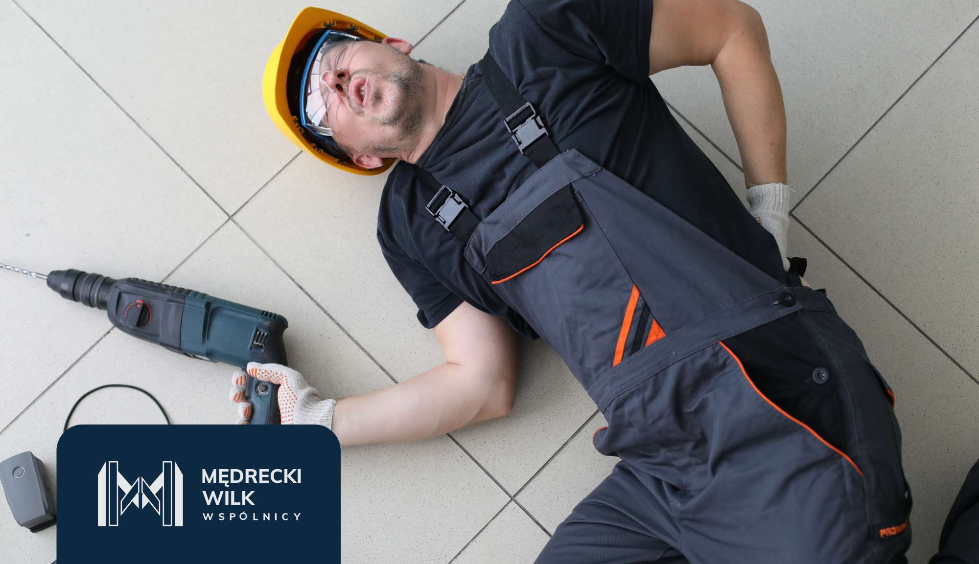 Construction worker in dark overalls and a yellow helmet lying on a tiled floor with a power drill nearby and a dark blue company logo overlay in the corner.