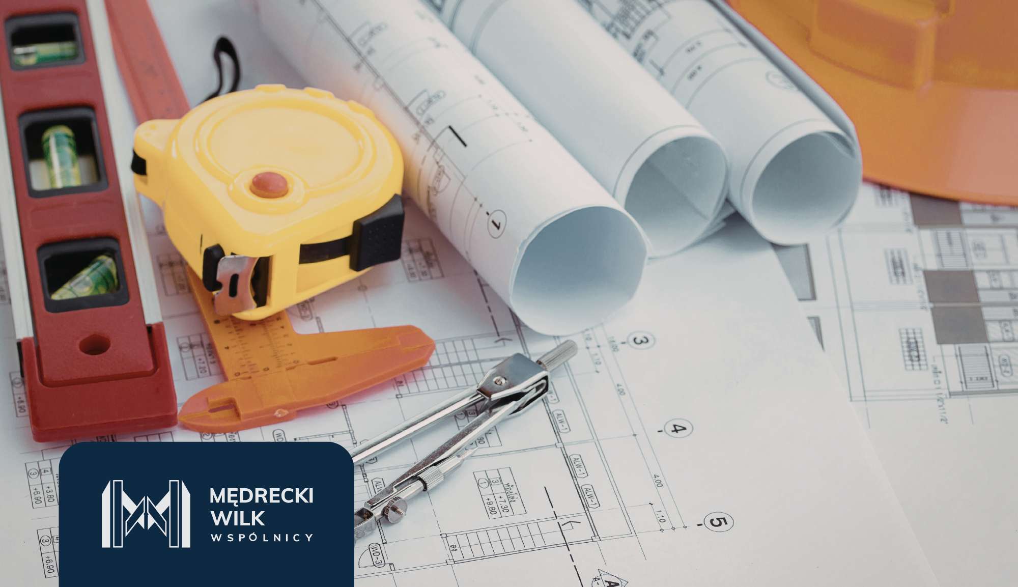 Construction workspace with rolled blueprints, a yellow tape measure, level, and drafting tools spread across plans, plus a company logo in the corner.