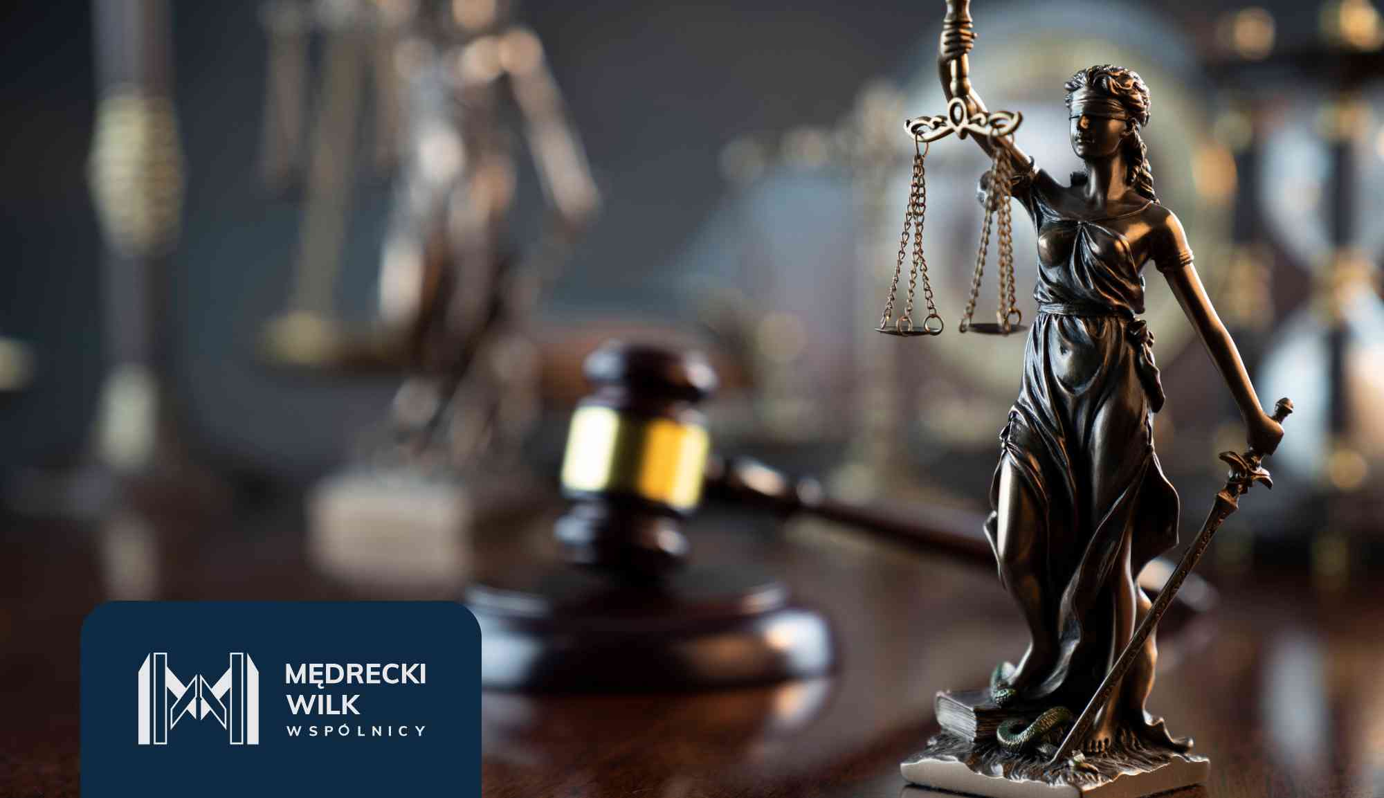 Bronze scales of justice in focus with a blurred person signing documents in the background; law firm branding visible at the bottom left.