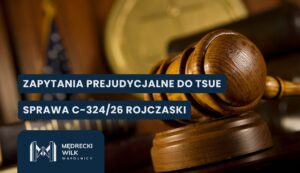Zbliżenie na jasnobrązowy, drewniany młotek sędziowski spoczywający na podstawce, ustawiony z prawej strony kadru. W rozmytych odcieniach brązu i złota w tle widoczny jest okrągły medalion oraz fragmenty książek. Na grafikę nałożone dwa granatowe paski z białymi napisami: „ZAPYTANIA PREJUDYCJALNE DO TSUE” oraz „SPRAWA C-324/26 ROJCZASKI”. W lewym dolnym rogu logotyp kancelarii Mędrecki Wilk i Wspólnicy.