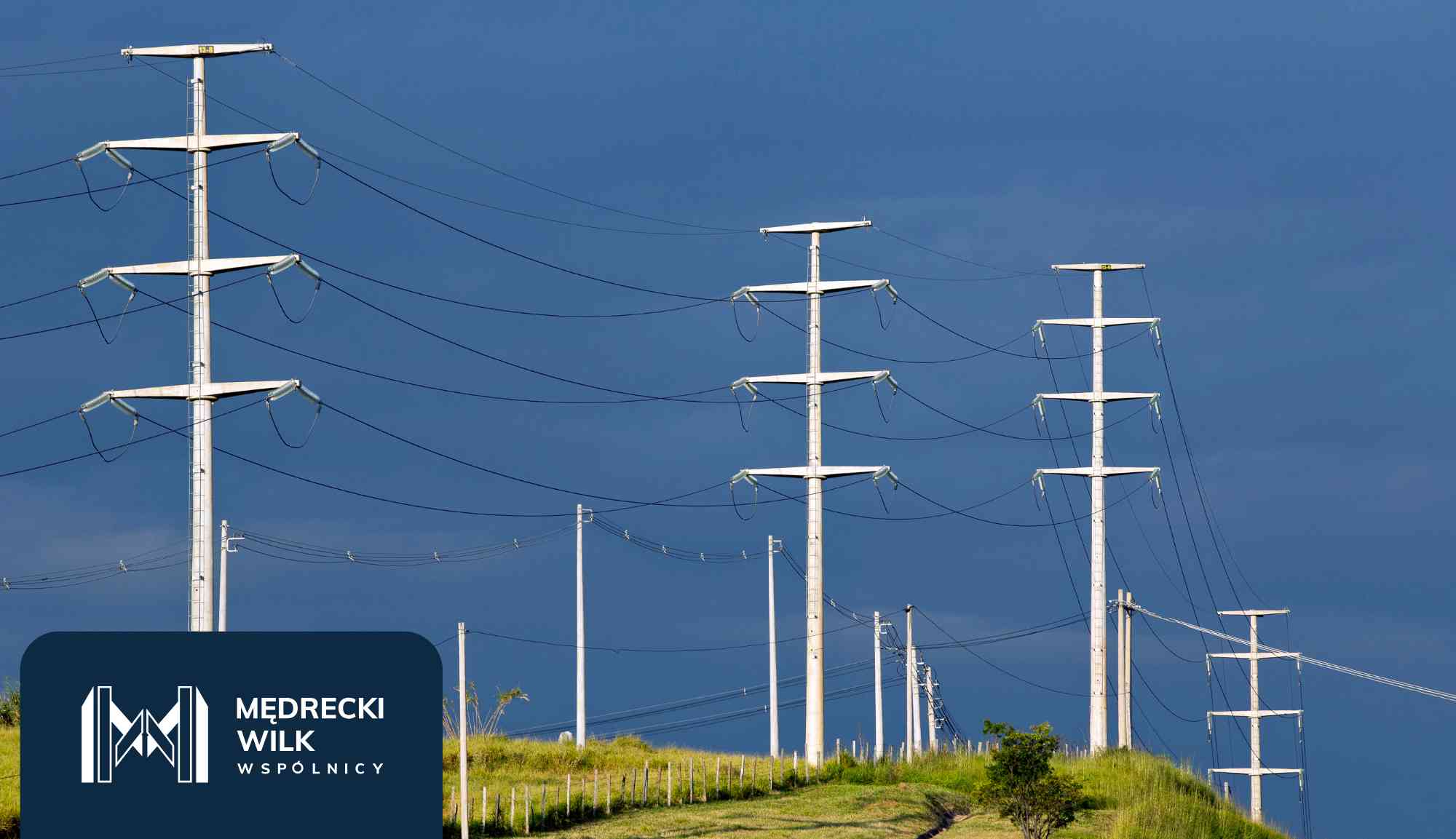 Power lines and tall transmission towers silhouetted against a colorful sunset sky, with a dark blue overlay and company logo in the lower-left corner reading 'Medrecki Wilk Wspólnicy'