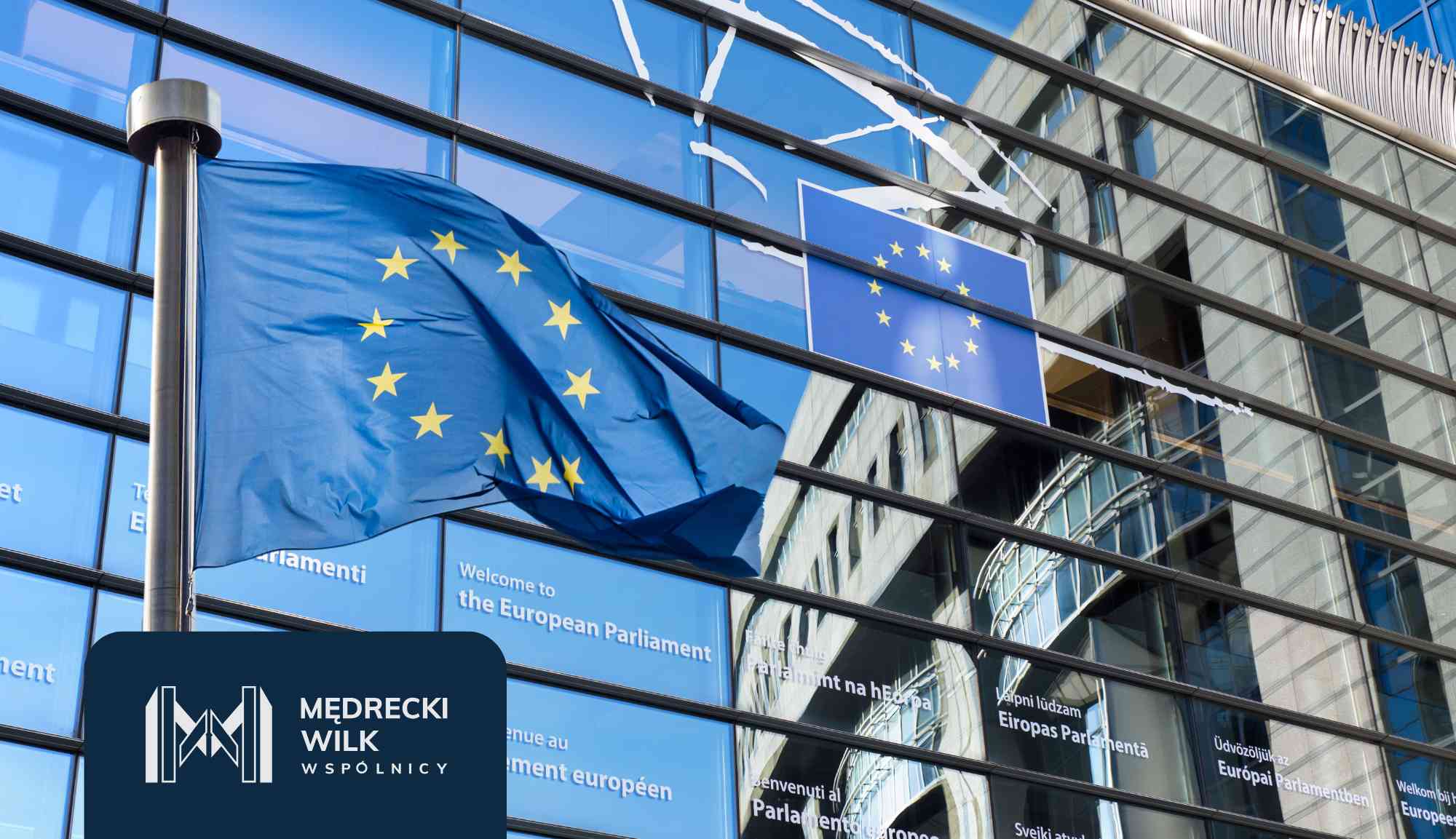 EU flag waving in front of a modern glass European Parliament building with multilingual signage in the windows.