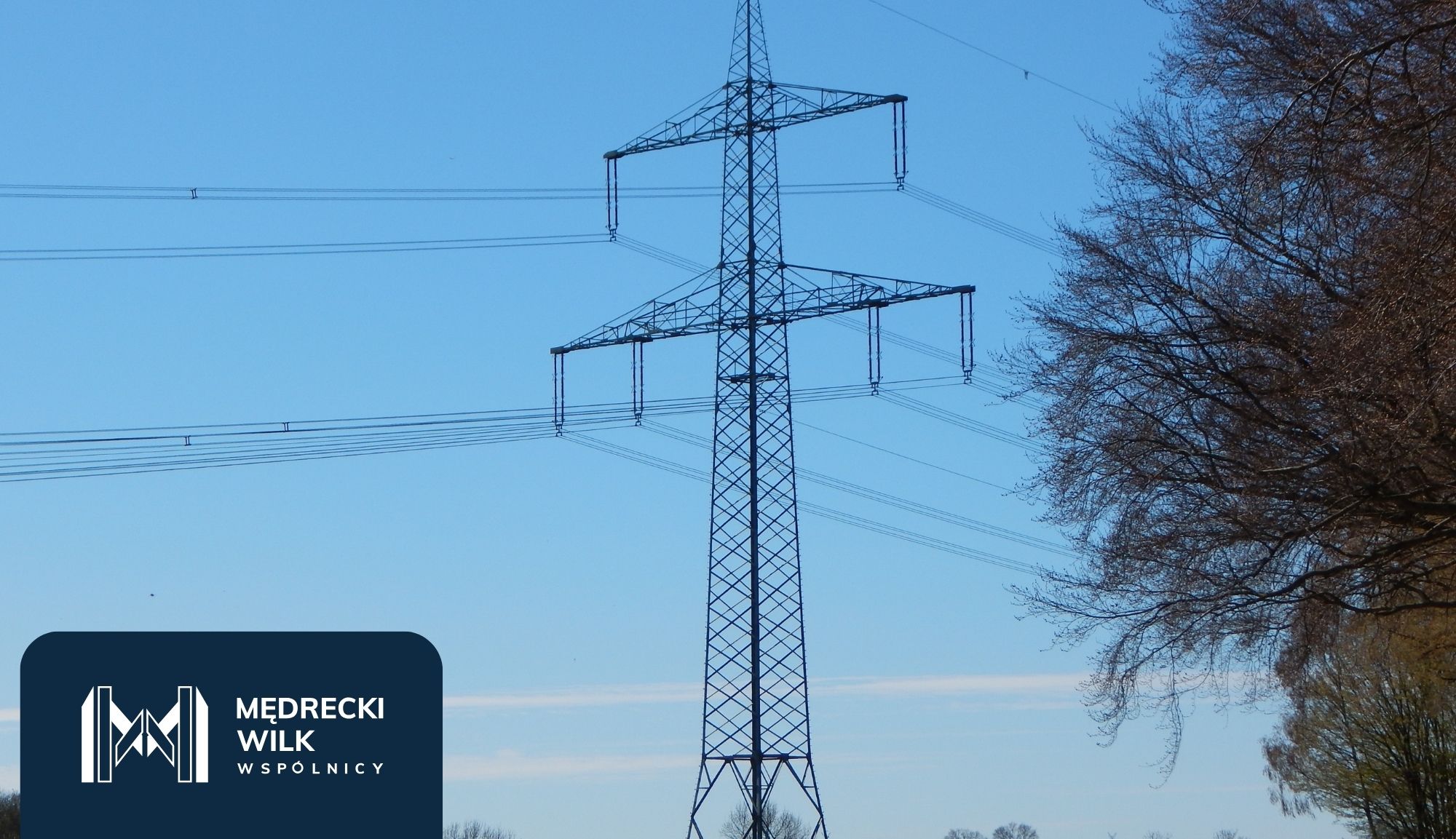 Power lines and tall transmission towers silhouetted against a colorful sunset sky, with a dark blue overlay and company logo in the lower-left corner reading 'Medrecki Wilk Wspólnicy'