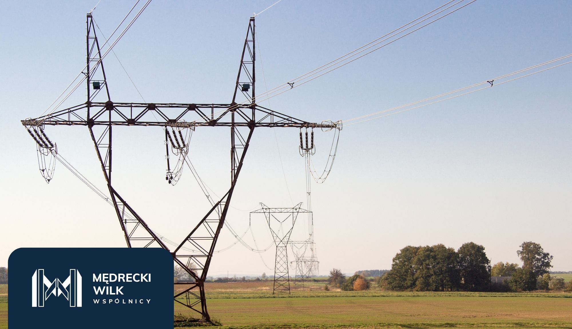 Power lines and tall transmission towers silhouetted against a colorful sunset sky, with a dark blue overlay and company logo in the lower-left corner reading 'Medrecki Wilk Wspólnicy'